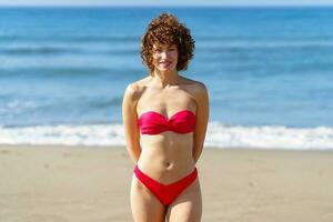 leende kvinna i röd bikini på strand foto