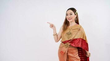 asiatisk kvinna bär typisk, traditionell thai klänning med identitet thai kultur pekande finger bort på kopia Plats isolerat över vit bakgrund foto