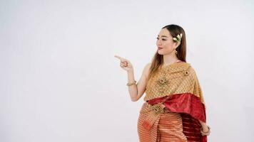 asiatisk kvinna bär typisk, traditionell thai klänning med identitet thai kultur pekande finger bort på kopia Plats isolerat över vit bakgrund. känsla leende foto