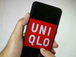 jakarta, Indonesien, 2023. hand innehav mobil telefon med finger Rör de uniqlo logotyp på skärm. foto