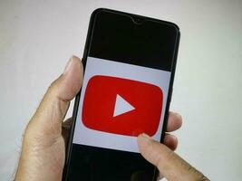 jakarta, Indonesien, 2023. hand innehav mobil telefon med finger Rör de Youtube logotyp på skärm. foto