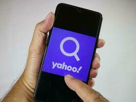 jakarta, Indonesien, 2023. hand innehav mobil telefon med finger Rör de yahoo logotyp på skärm. foto