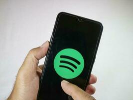 jakarta, Indonesien, 2023. hand innehav mobil telefon med finger Rör de Spotify logotyp på skärm. foto