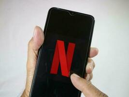 jakarta, Indonesien, 2023. hand innehav mobil telefon med finger Rör de Netflix logotyp på skärm. foto