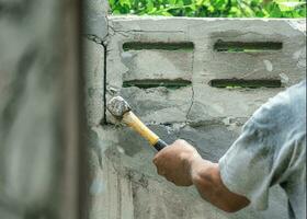 hand av arbetstagare använder sig av hammare krossar och förstöra på tegel vägg på konstruktion webbplats foto
