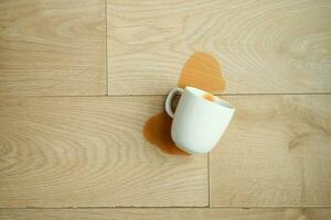 kopp av kaffe spillts på trä- golv foto