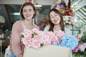 porträtt av två ung skön kvinna florister med blommig knippa leverans, leende och ser på kamera, härlig företag entreprenör, blomma affär Lycklig arbete, ljust färgrik flora bukett Lagra. foto
