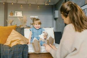 mamma sätter på henne dotters tofflor medan Sammanträde på de soffa i de hus foto