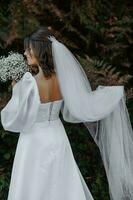 en romantisk brud i en skön klänning innehar en slöja i ett hand och en bukett av skön Gypsophila i de Övrig. foto