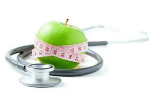 mätning tejp insvept runt om en grön äpple med stetoskop isolerat på vit foto