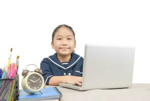 liten asiatisk flicka håller på med läxa med bärbar dator uppkopplad isolerat på vit bakgrund, foto