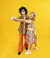 asiatisk hippie par klänning i 80s årgång mode med färgrik retro Kläder medan dans tillsammans isolerat på gul bakgrund för fint utrusta fest och pop- kultur begrepp foto