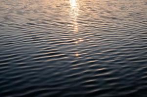 solsken glödande på krusat vatten i sjön på morgonen foto