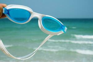 hand innehar simning glasögon mot havsbild. tropisk semester begrepp. foto