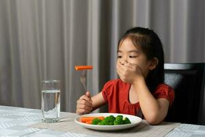 liten söt unge flicka vägrar till äta friska grönsaker. barn do inte tycka om till äta grönsaker. foto