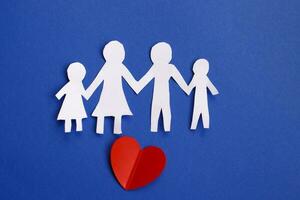Lycklig papper skära familj innehav händer på blå bakgrund med röd hjärta. foto
