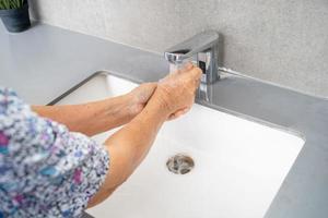 asiatisk senior eller äldre gammal dam kvinna patient tvätta handen med tvål och rent vatten för att skydda säkerhetsinfektion och döda roman coronavirus covid 19 virus foto