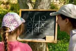 mor och dotter i de trädgård spelar luffarschack på en skiffer styrelse. foto