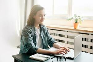 ung kvinna använder sig av bärbar dator dator i en modern kontor miljö och studerande flicka arbetssätt från de bekvämlighet av Hem. uppkopplad arbete, studie, frilans, företag, och kontor livsstil begrepp foto
