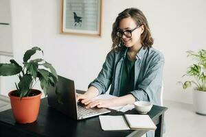 ung kvinna arbetssätt på bärbar dator i professionell kontor miljö. studerande flicka göra flera saker samtidigt på Hem kontor. arbeta hemifrån, frilans, företag livsstil begrepp. teknologi, produktivitet och avlägsen arbete. foto