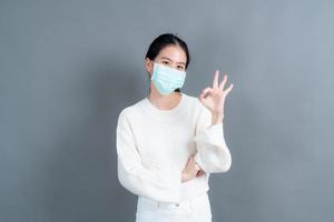 ung asiatisk kvinna som bär medicinsk ansiktsmask och visar ok tecken foto