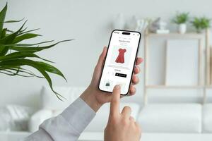 kvinna handla uppkopplad med smart telefon. uppköp en röd strömma klänning på e-handel webb sida. levande rum interiör i bakgrund foto