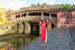kvinna resande bär ao dai vietnamese klänning sightseeing på japansk täckt bro i hoi ett stad, vietnam. landmärke och populär för turist attraktioner. vietnam och sydöst Asien resa begrepp foto