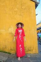 Lycklig kvinna bär ao dai vietnamese klänning och hatt, resande sightseeing på hoi ett gammal stad i central vietnam. landmärke och populär för turist attraktioner. vietnam och sydöst resa begrepp foto