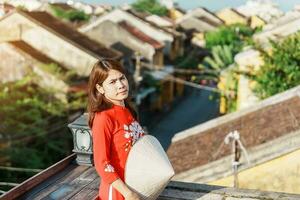 Lycklig kvinna bär ao dai vietnamese klänning, resande sightseeing se på taket på hoi ett gammal stad i vietnam. landmärke och populär för turist attraktioner. vietnam och sydöst resa begrepp foto