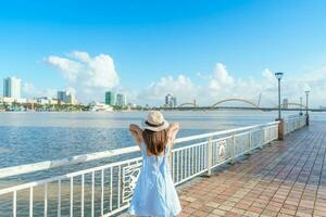 kvinna resande med blå klänning besöker i da nang stad. turist sightseeing de flod se med drake bro. landmärke och populär för turist attraktion. vietnam och sydöst Asien resa begrepp foto