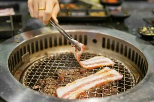 hand grillning kött fläsk på spis tjäna i restaurang. japansk mat och koreanska bbq traditionell stil foto