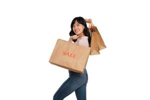 ung Lycklig asiatisk kvinna med tillfällig skjorta och denim jeans innehav handla papper väska isolerat på vit bakgrund foto