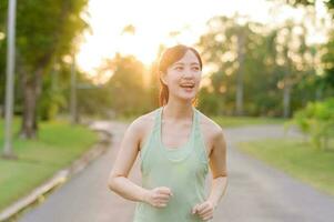 passa asiatisk ung kvinna joggning i parkera leende Lycklig löpning och njuter en friska utomhus- livsstil. kvinna joggare. kondition löpare flicka i offentlig parkera. friska livsstil och wellness varelse begrepp foto