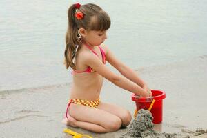 flicka spelar med sand på de hav Strand foto