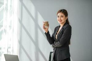 ung leende asiatisk företag kvinna entreprenör, elegant professionell företag chef, framgångsrik affärskvinna verkställande ledare bär kostym stående i modern kontor. vertikal porträtt foto