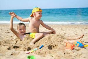 bror och syster spela på de strand med plast leksaker med sand.barn är spelar på de strand. sommar vatten roligt för de hela familj. en pojke och en flicka är spelar med sand på de stranden. foto