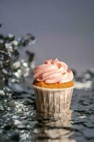 en muffin med en rosa keps står bland de flygande silver- konfetti. foto