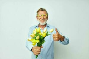 senior gråhårig man en bukett av blommor med glasögon som en gåva ljus bakgrund foto