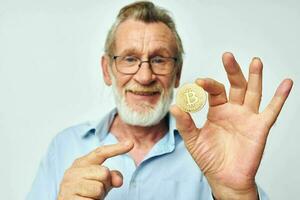 senior gråhårig man finansiera guld mynt bitcoin Framställ ljus bakgrund foto
