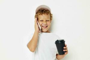 söt pojke i en vit t-shirt keps med en telefon i en glas med en dryck livsstil oförändrad foto