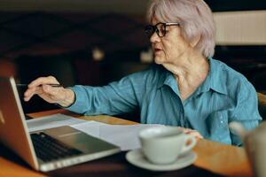 skön mogna senior kvinna arbetssätt i främre av bärbar dator övervaka Sammanträde pensionerad kvinna chattar oförändrad foto