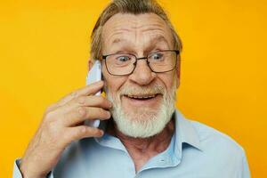 gammal man i en blå skjorta och glasögon talande på de telefon gul bakgrund foto