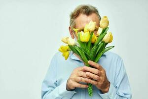 gammal man i en blå skjorta med en bukett av blommor ljus bakgrund foto