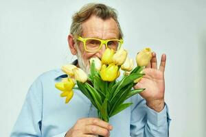 porträtt av Lycklig senior man en bukett av blommor med glasögon som en gåva ljus bakgrund foto