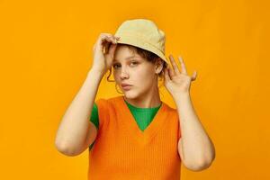 söt flicka bär hatt Framställ orange Tröja isolerat bakgrund foto