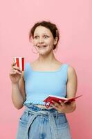 glad kvinna innehav en anteckningsbok i henne händer disponibel glas dryck rosa bakgrund oförändrad foto