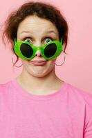 skön kvinna i en rosa t-shirt grön glasögon ungdom mode rosa bakgrund foto