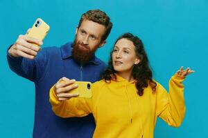 kvinna och man rolig par med telefoner i hand tar selfies krokig leende roligt, på blå bakgrund. de begrepp av verklig familj relationer, talande på de telefon, arbete uppkopplad. foto