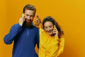 kvinna och man glad par med telefoner i hand talande på cell telefon krokig leende glad, på gul bakgrund. de begrepp av verklig familj relationer, talande på de telefon, arbete uppkopplad. foto