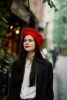 kvinna leende mode modell promenader på de gata i de stad Centrum bland de folkmassan i en jacka och röd basker och jeans, filmiska franska mode stil Kläder, resa till istanbul vår foto